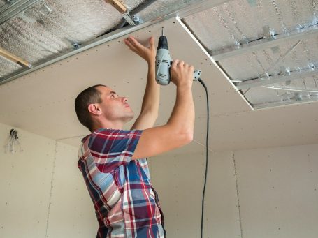 Installer fitting plasterboard to ceiling
